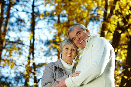 Photo of amorous aged man and woman looking at camera in autumnal park