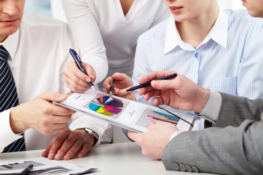 Image of several hands of working partners discussing business charts