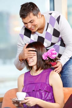 Happy man with bunch of flowers shutting eyes of young female in cafe