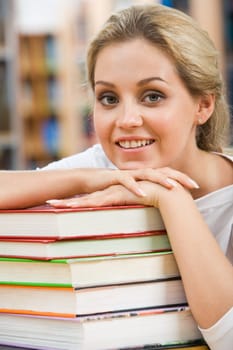 Portrait of pretty student putting her chin on hand over pile of books