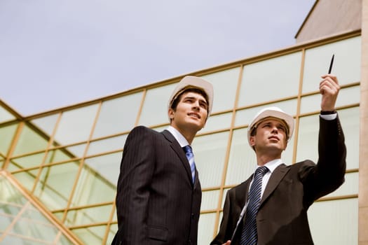 Photo of serious employee pointing at something with confident foreman standing near by