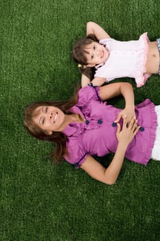 Happy child and her mother lying on green grassland and looking at camera with smiles
