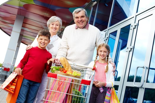 Portrait of happy grandparents and grandchildren with package of food near supermarket