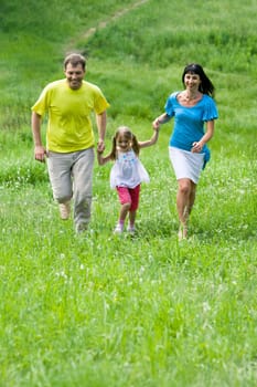 Photo of happy people outdoors holding each other by hands and running down green grass