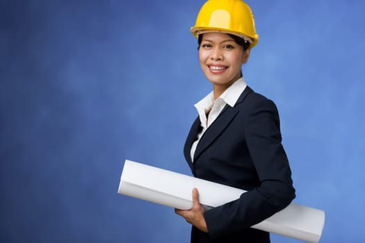 Portrait of pretty female with blueprints in hands and helmet on head smiling