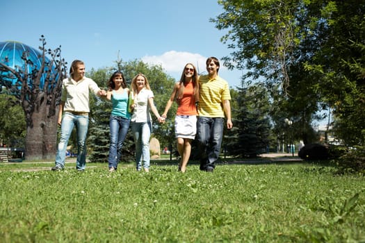Photo of cheerful friends walking down green grass in park and chatting