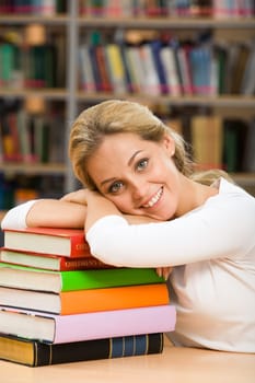 Photo of smiling teacher putting her head over stack of books and looking at camera