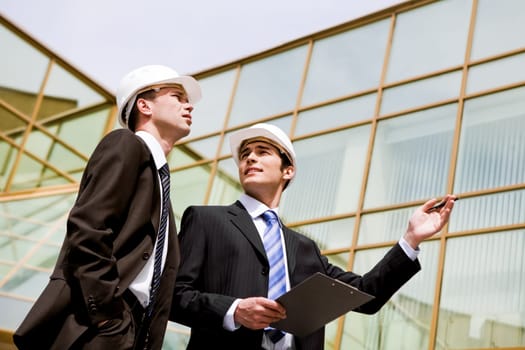 Photo of two co-workers discussing new project with modern building at background