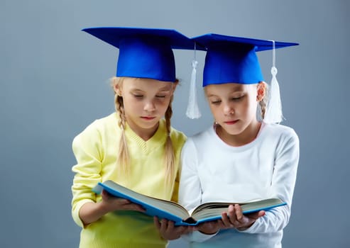 Portrait of lovely twin girls in hats with tassels reading book