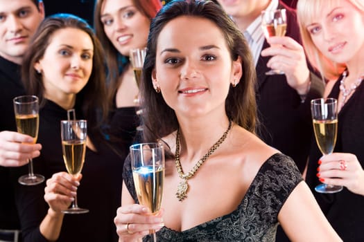 Fascinating woman is holding the alcoholic drink on the background of her friends