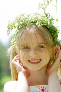 Close-up of small cute girl wearing floral wreath looking at camera