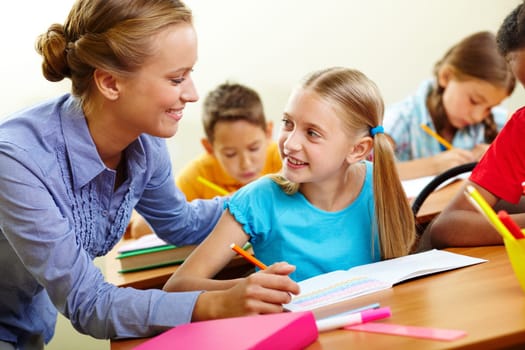 Portrait of smart girl and her teacher looking at each other at lesson in classroom