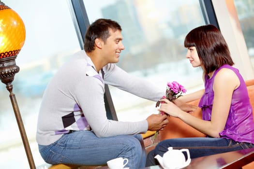 Happy man giving bunch of flowers to young female in cafe