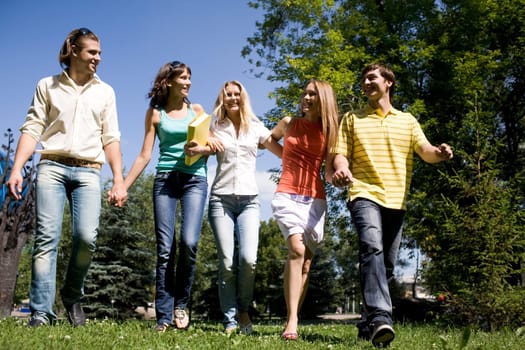 Photo of cheerful friends walking down green grass in park and chatting