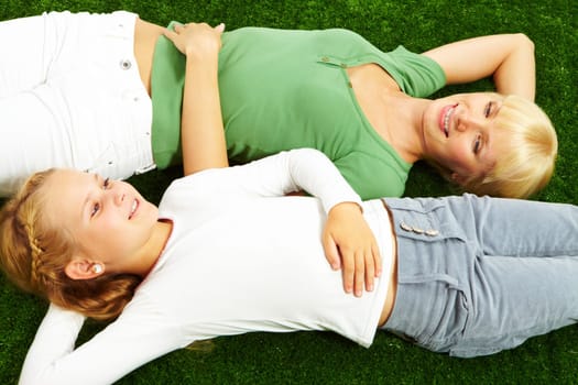 Portrait of happy woman and her pretty daughter relaxing on green grass
