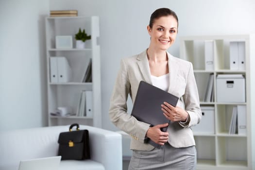Portrait of smiling businesswoman with folder looking at camera in office