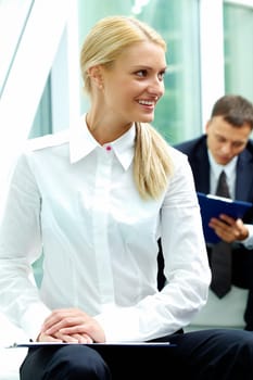 Confident businesswoman looking aside at background of reading man