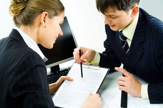 Close-up of two confident colleagues looking at document attentively while man pointing at some piece of text in it with pencil