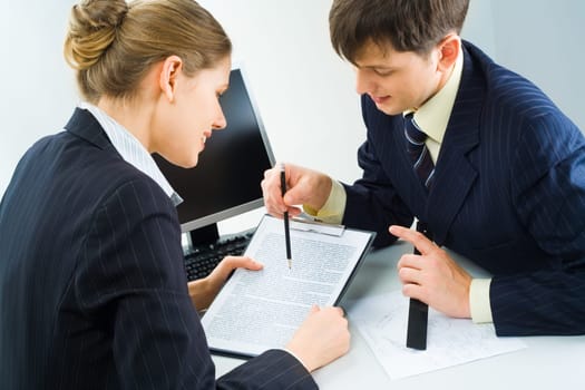 Two business partners sitting at the table and looking at the contract with a laptop at the backgrounds