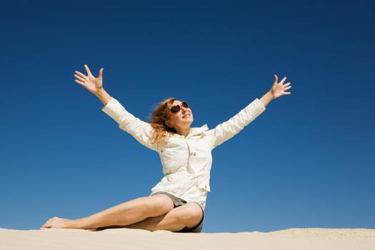 Image of joyful female in casual clothes sitting on sand and enjoying herself
