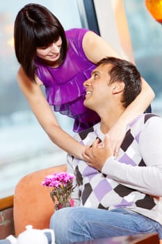 Happy girl embracing handsome man with bunch of flowers in cafe