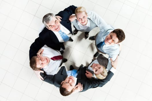 Above view of several business partners looking upwards at camera while embracing each other