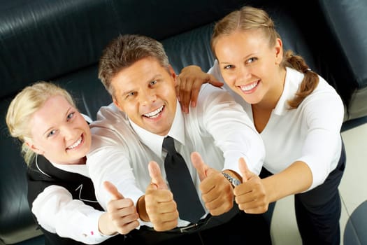 Image of company of successful partners showing thumbs up and looking at camera