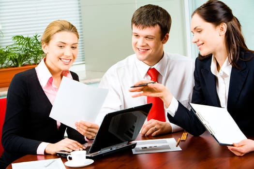 Portrait of three businesspeople working at the table in the office looking into document in womans hand