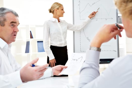 Image of successful businesswoman standing by whiteboard while her colleagues listening to her