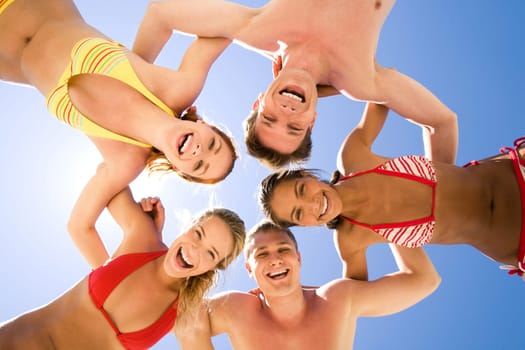Circle of joyful teenagers hugging each other during summer vacations and looking at camera