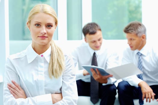 Confident businesswoman looking at camera at background of communicating men