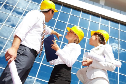 Below view of business partners in helmets looking at modern office building