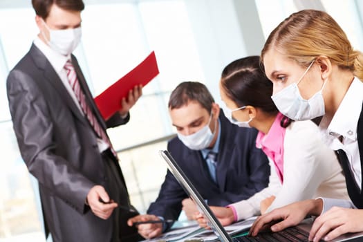 Serious businesswoman in protective mask looking at screen of laptop in working environment