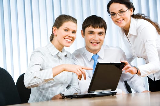 Team of three businesspeople gathered around the table with laptop and working