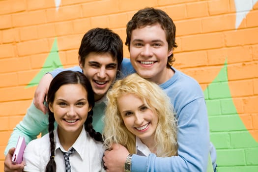 Portrait of glad friends in casual clothes looking at camera on background of brick wall