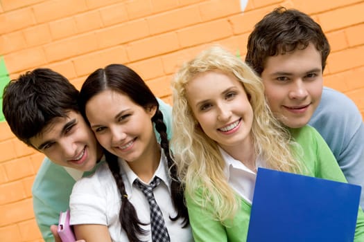 Portrait of friendly students looking at camera with happy smiles on background of brick wall