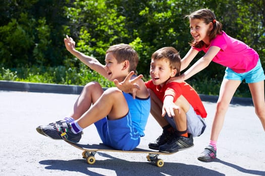 A girl pushing skateboard with two boys sitting on it