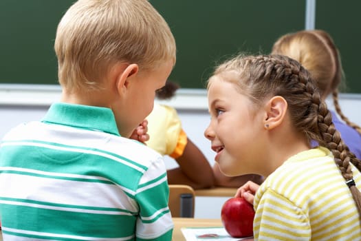 Portrait of schoolchildren sitting in classroom and chatting at lesson