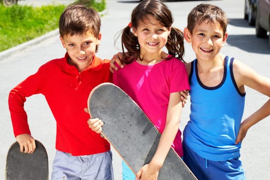 Portrait of three embracing children with skateboards looking at camera and smiling
