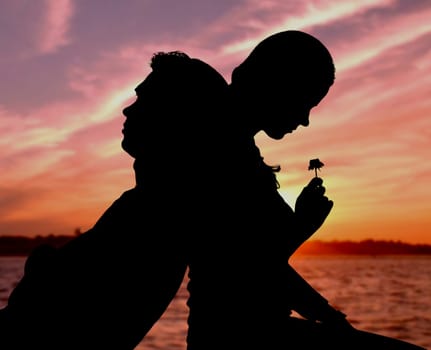 Silhouette of couple sitting back to back on background of sunset