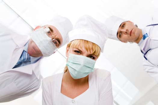 Image of pretty nurse in mask looking at camera with her colleagues at background