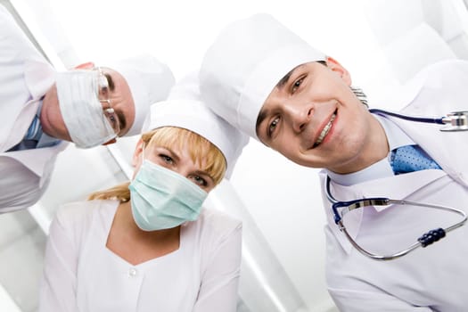 Below view of happy doctors with nurse between them looking at camera