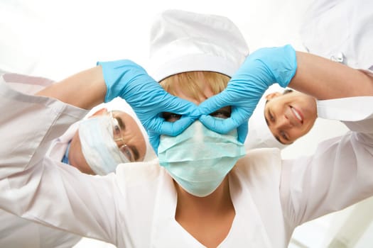 Image of nurse in mask keeping her gloved hands in front of her eyes with colleagues at background