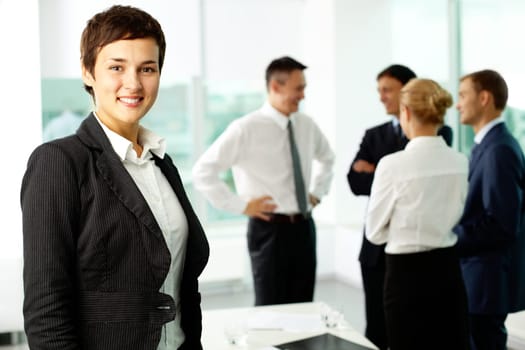 Attractive businesswoman looking at camera and smiling aginst her colleagues