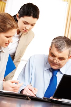 Image of serious businessman signing contract with two females near by