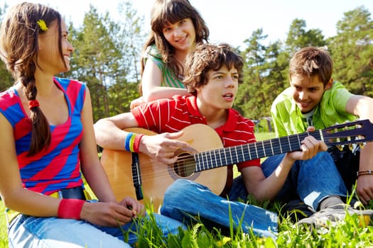 Portrait of handsome lad playing the guitar surrounded by his friends