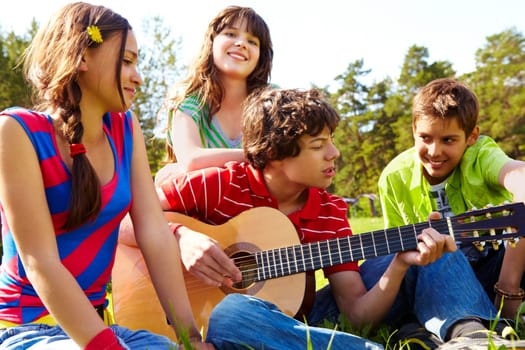 Portrait of handsome lad playing the guitar surrounded by his friends