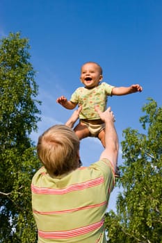 Photo of happy man throwing his cute son up in the forest