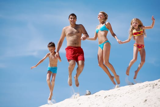 Photo of happy family jumping on sand on summer vacation