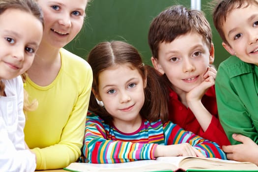 Portrait of five pupils looking at camera with open book near by